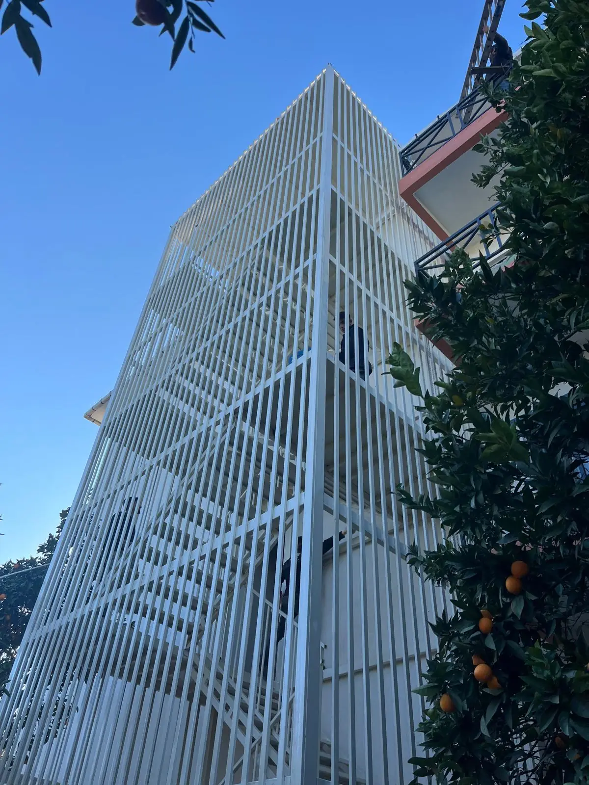 Stair tower with a white steel lamella façade against a blue sky.