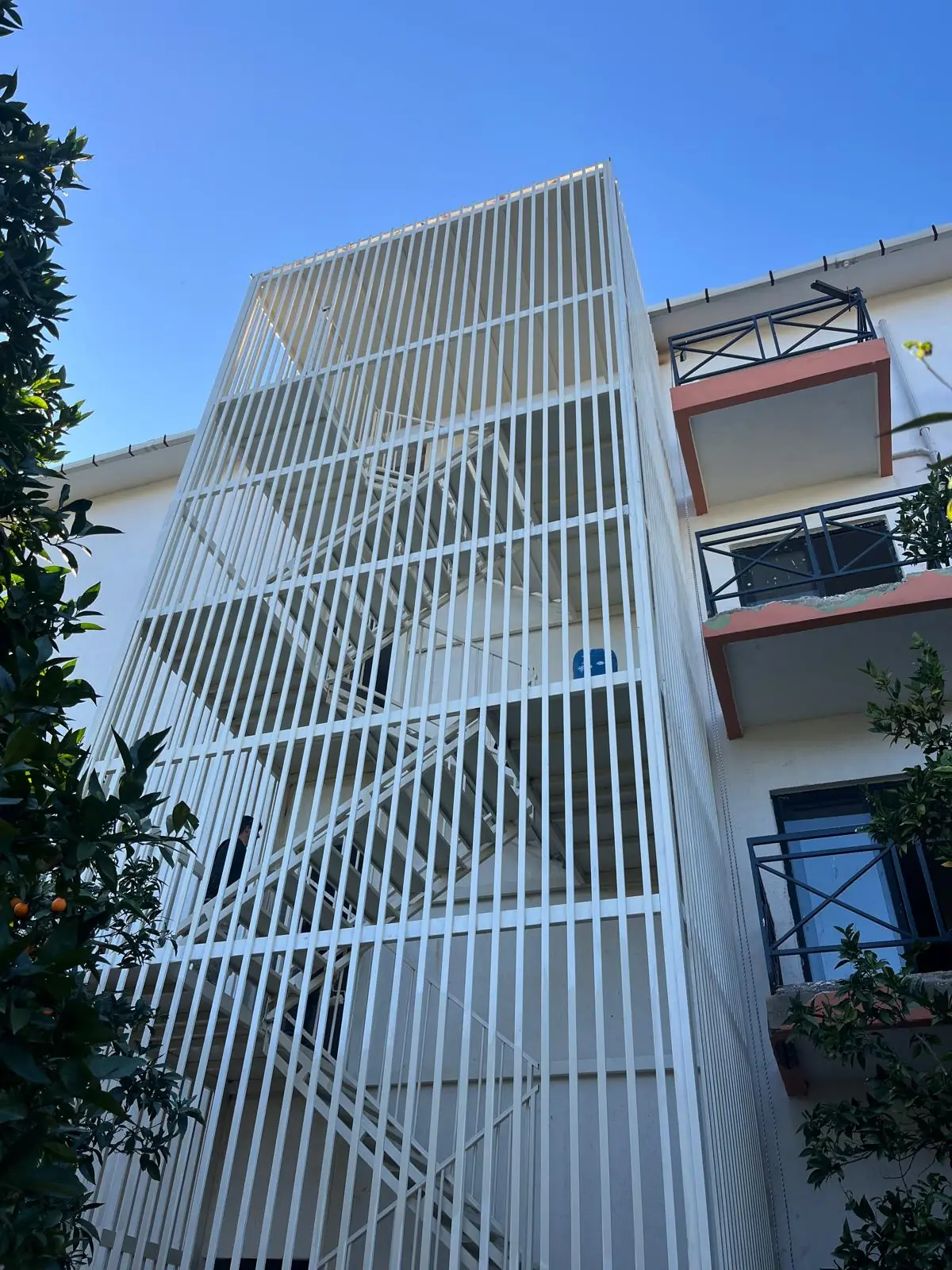 The lamella stair tower seen between orange trees.