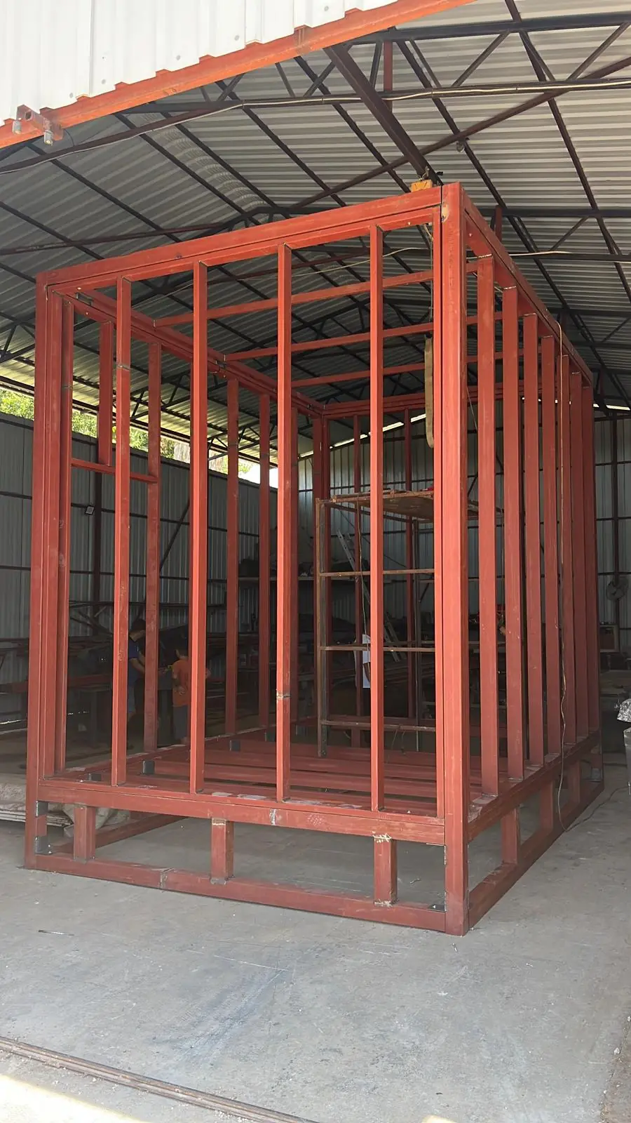 A red-primed steel frame module under cover.