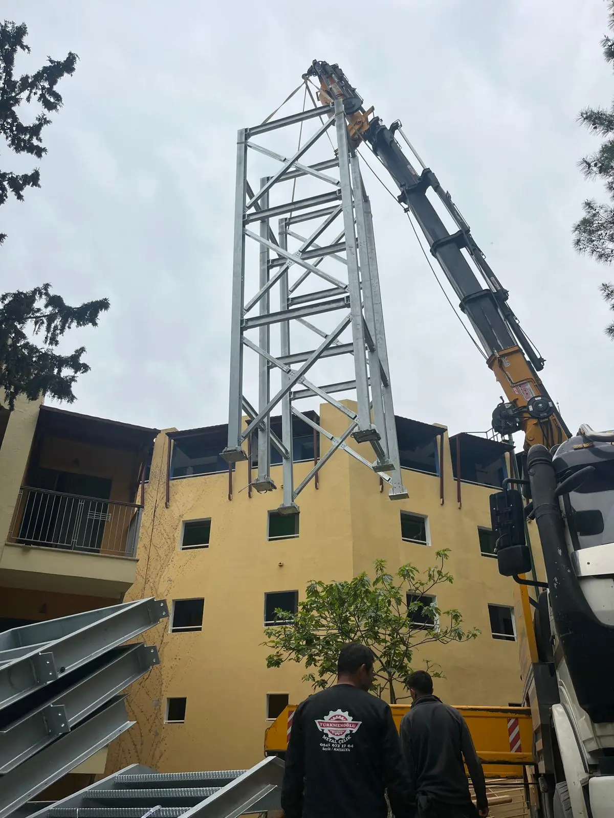 A crane setting a steel tower beside the roofline, with the Türkmenoğlu crew in front.